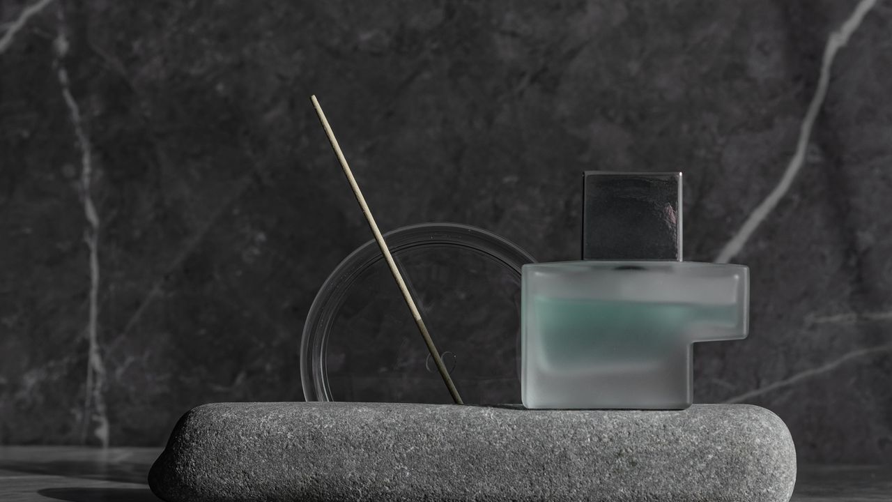 A single glass perfume bottle standing on a stone slab in soft light